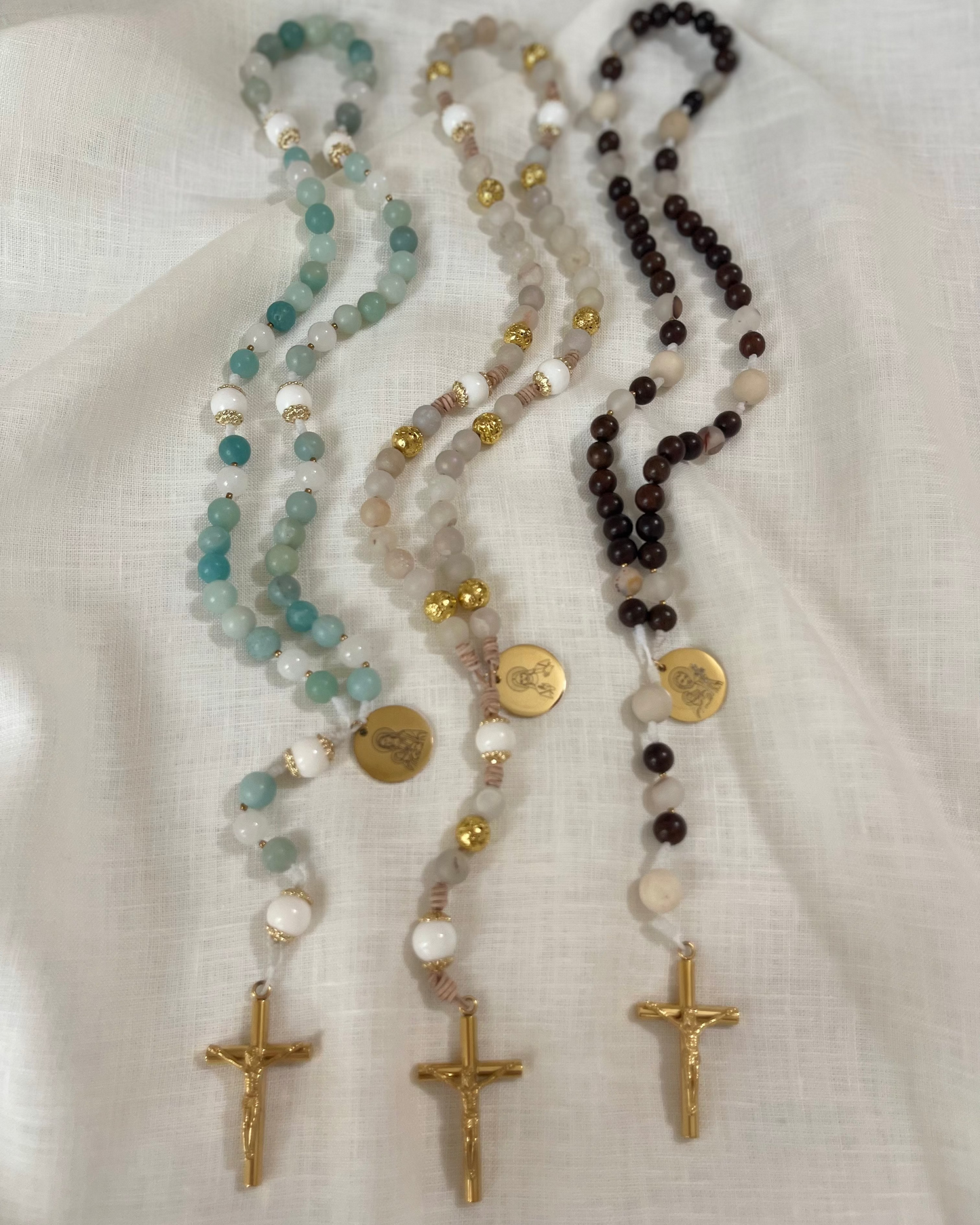 The Holy Family Inaugural Collection featuring The Mary, The Jesus, and The Joseph handmade Catholic rosaries arranged vertically side-by-side on white linen.