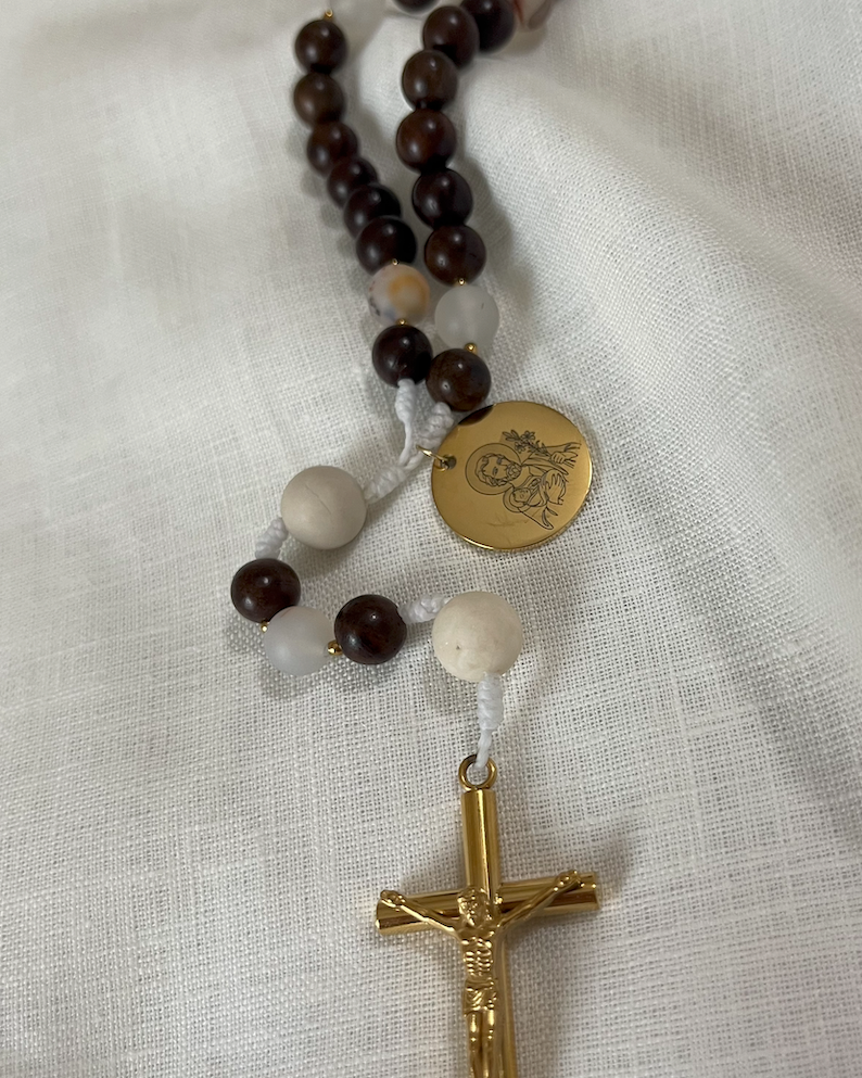 Close-up of a custom engraved gold Saint Joseph medal and a polished, tarnish-resistant gold crucifix attached to white hand-knotted cord.
