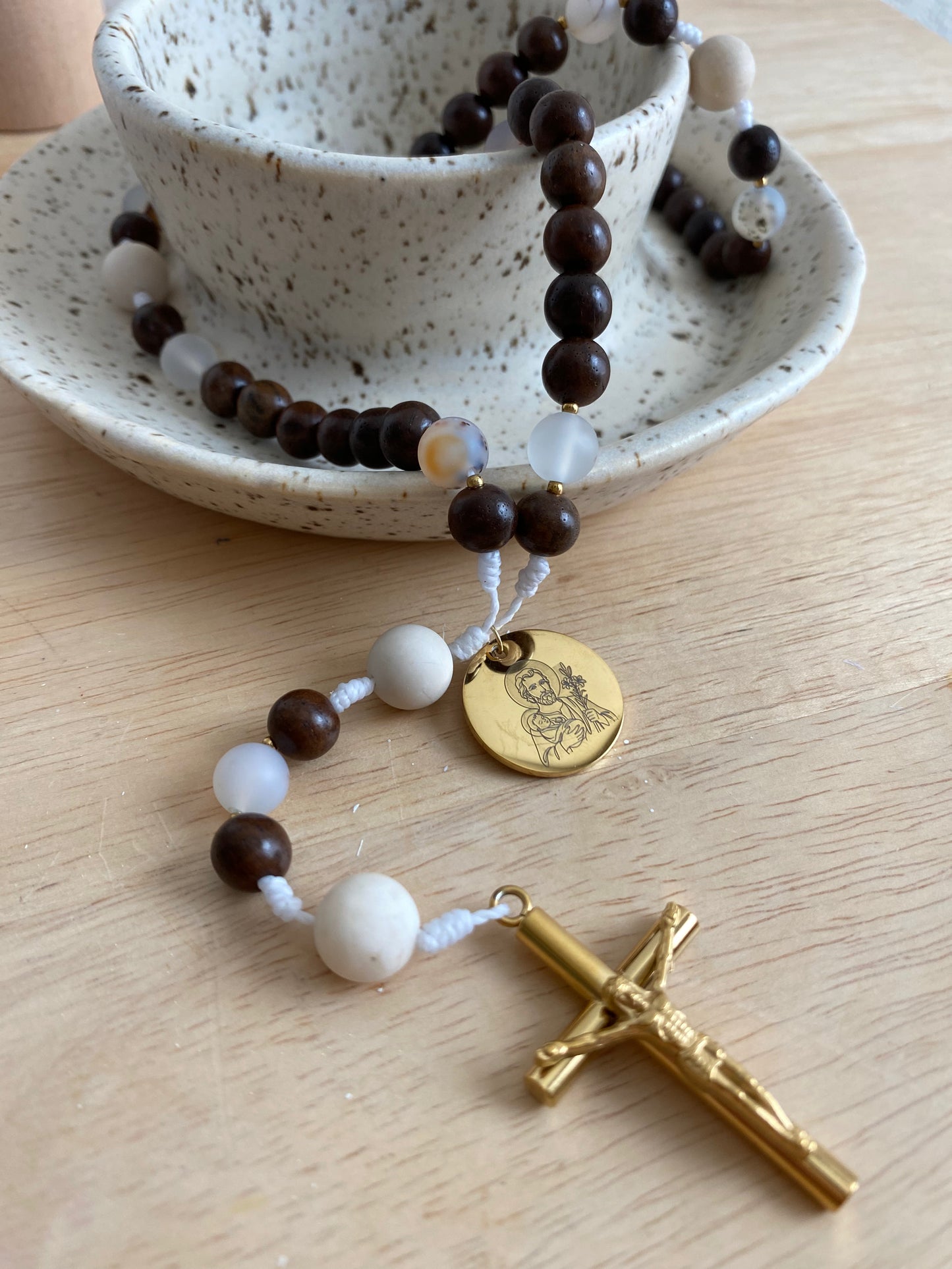 Detailed close-up view of semi-transparent jade and agate beads resting on a light wood surface next to a speckled ceramic dish.