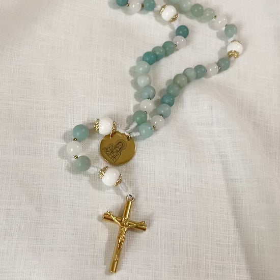 A slow, vertical loop video showcasing the complete length and subtle stone variations of The Mary gemstone rosary on a white cloth background.