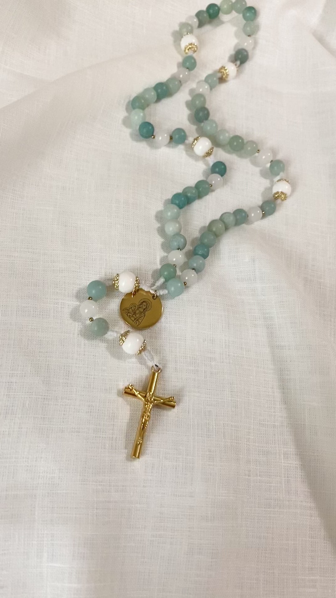 A slow, vertical loop video showcasing the complete length and subtle stone variations of The Mary gemstone rosary on a white cloth background.