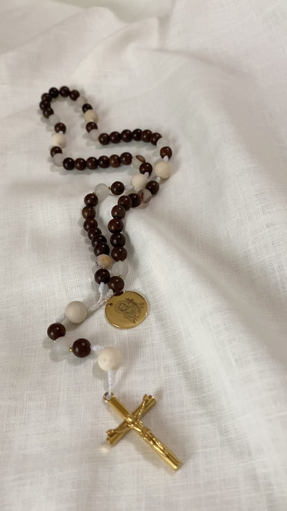 A close-up loop video showcasing the premium textures of The Joseph Catholic rosary, highlighting the smooth wood, detailed fossil jasper, and a gleaming gold Saint Joseph engraved medal on a textured white linen background.