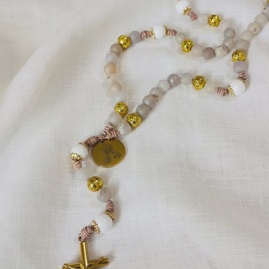 A slow vertical loop video showcasing the unique textures of gold lava stone, druzy, and white jade beads on a hand-knotted leather cord rosary.