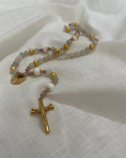 An artistic, close-up perspective focusing on a polished gold crucifix and detailed leather knots of The Jesus catholic rosary on a white linen fabric.