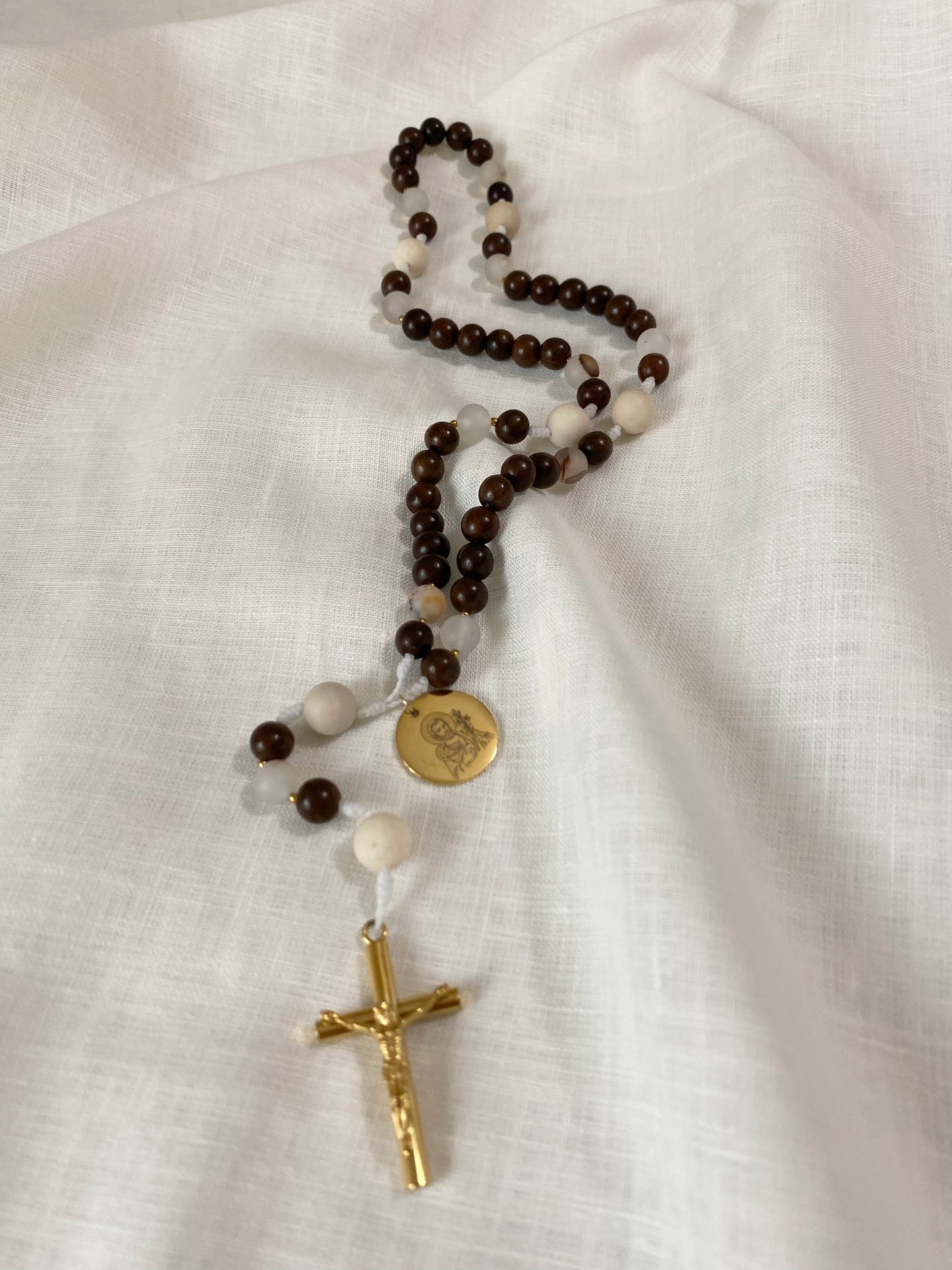 Handmade Catholic rosary with deep brown rosewood beads and neutral fossil jasper stones arranged on a textured white linen cloth.