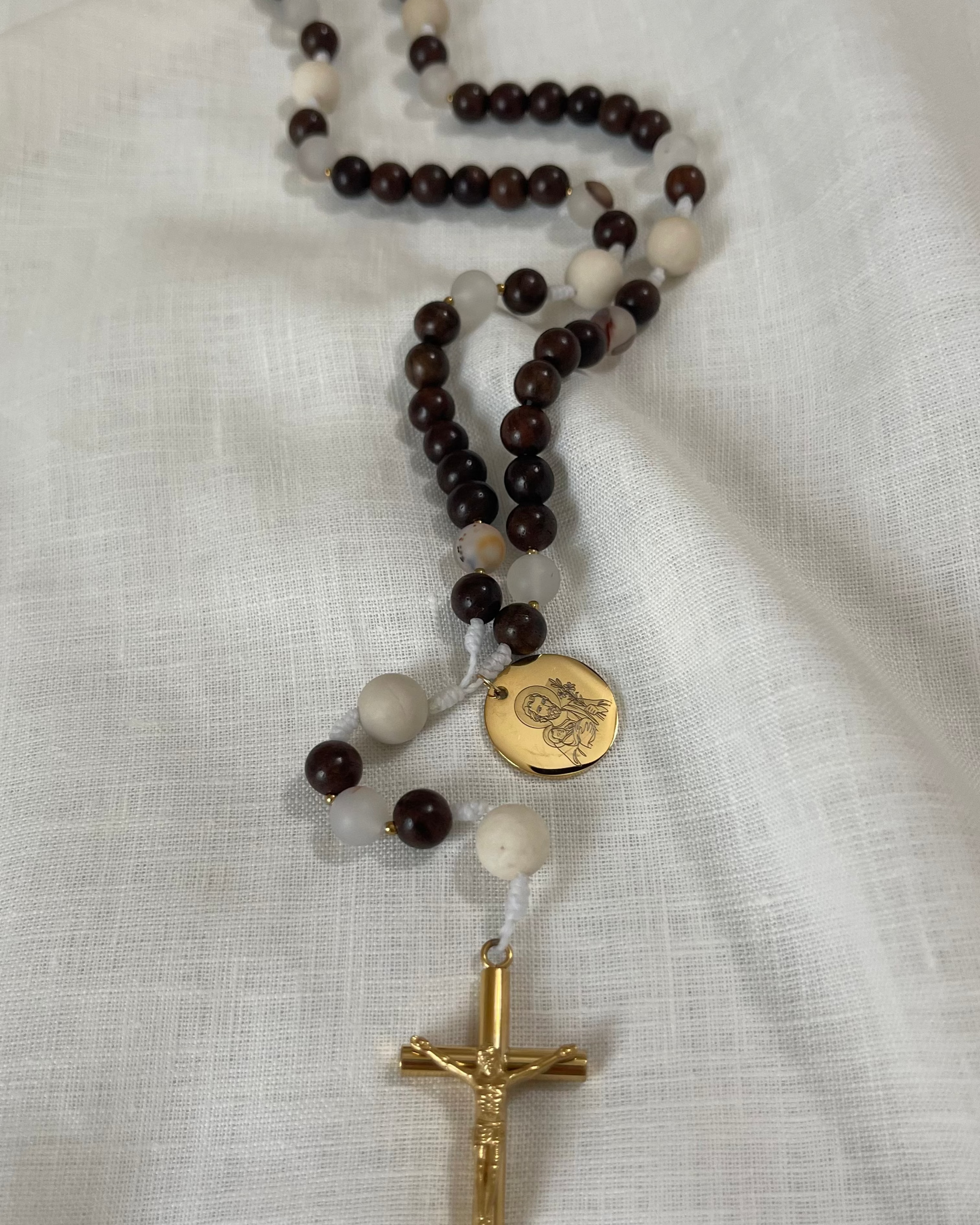 The Joseph Catholic rosary featuring organic wood beads, dendritic agate, and gold accents laid flat on a minimalist white linen background.